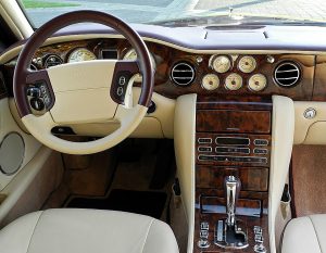 Luxurious car interior with wood panel dashboard, beige leather seats, and gear shifter visible.